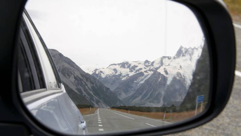 Side mirror of a car during a New Zealand road trip, with a view of snowy mountains.