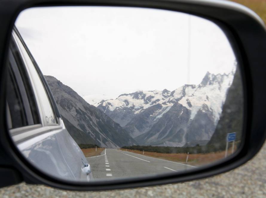 Side mirror of a car during a New Zealand road trip, with a view of snowy mountains.