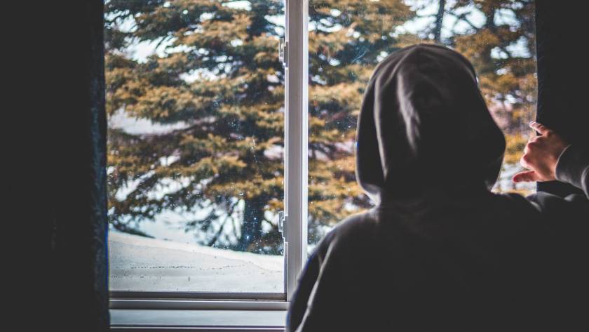 Kiwi man looking out of windows during winter, thinking about how to reduce the heating bill.