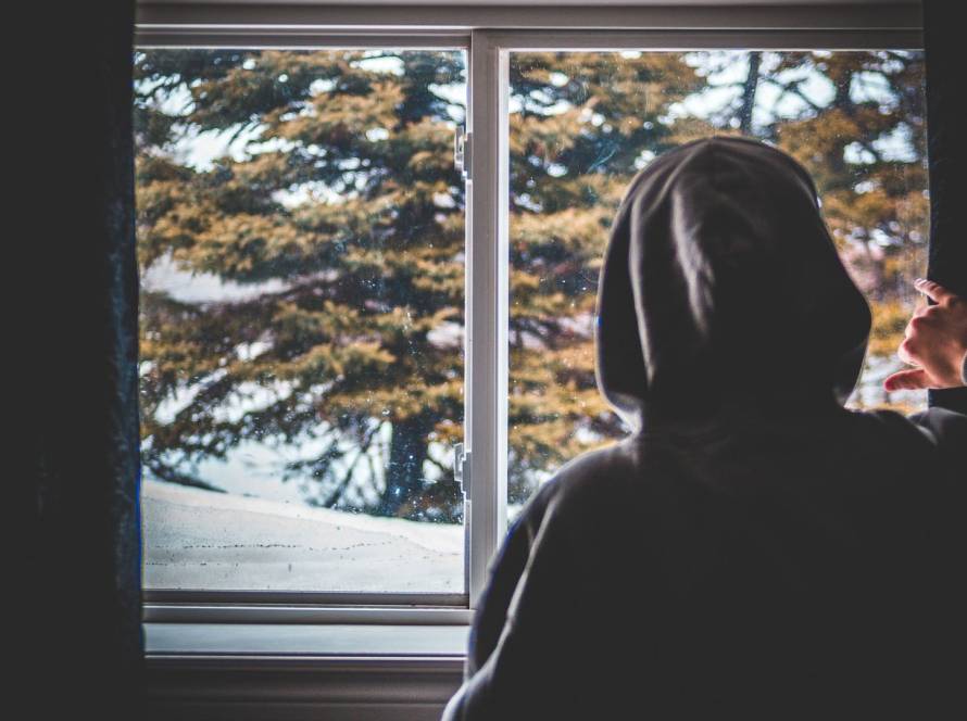 Kiwi man looking out of windows during winter, thinking about how to reduce the heating bill.